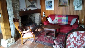 Una sala de estar acogedora con chimenea de piedra, un sofá rojo, sillas estampadas y una mesa de centro de madera.