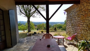Un patio cubierto con suelo de piedra, una mesa con mantel rojo y dos sillas.