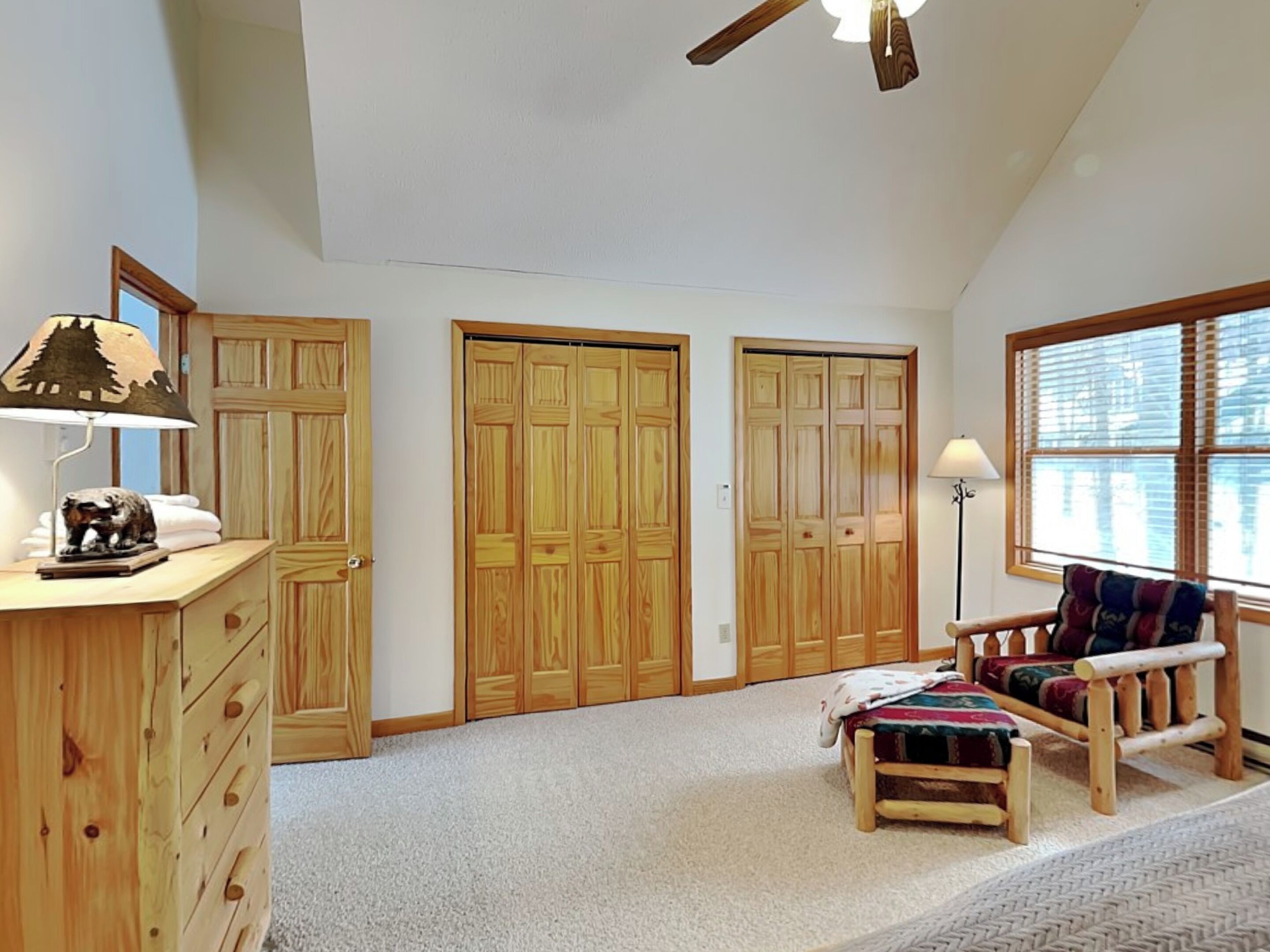 A spacious room with a large closet, a desk with a lamp, a chair, and a window with blinds.