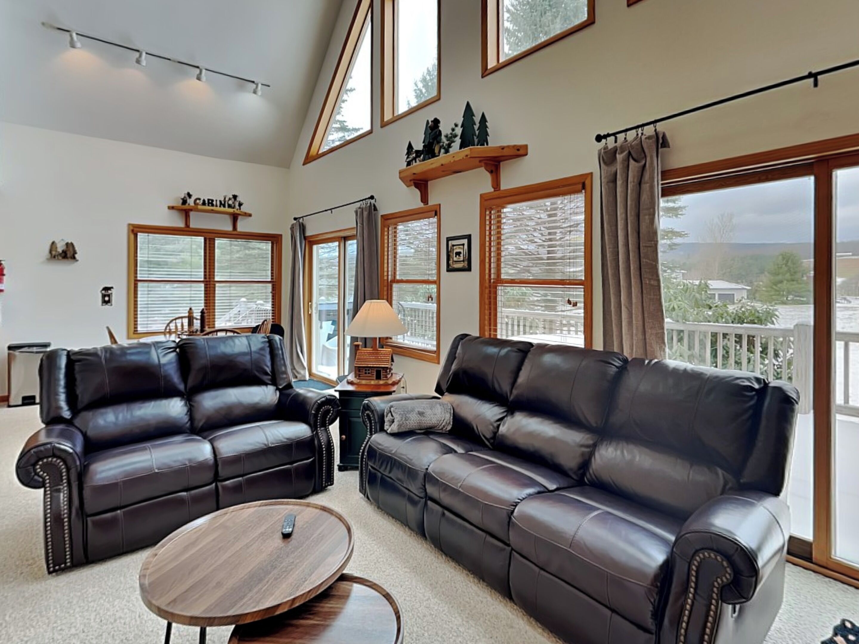 A spacious living room with two leather sofas, a round coffee table, and large windows offering a view of the outdoors.