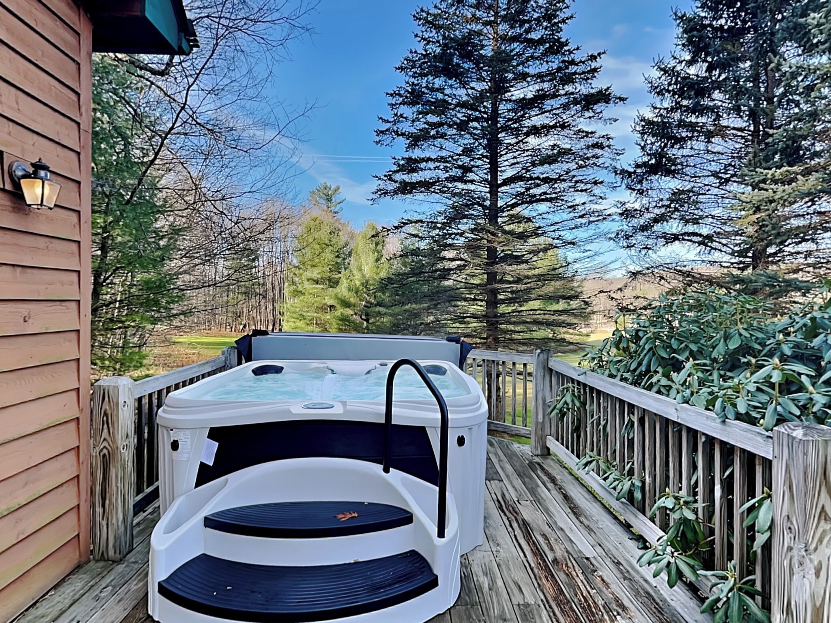 A hot tub on a wooden deck with a view of trees and a clear sky.