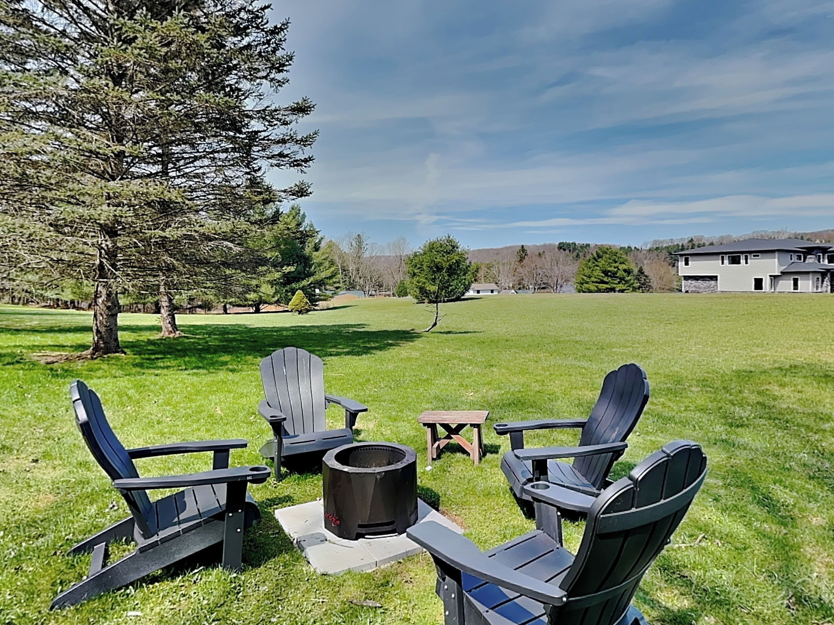 A grassy outdoor area with Adirondack chairs, a fire pit, and a small table.