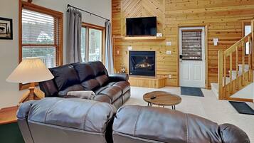 A cozy living room with a leather sofa, a small coffee table, a fireplace, and wooden walls.
