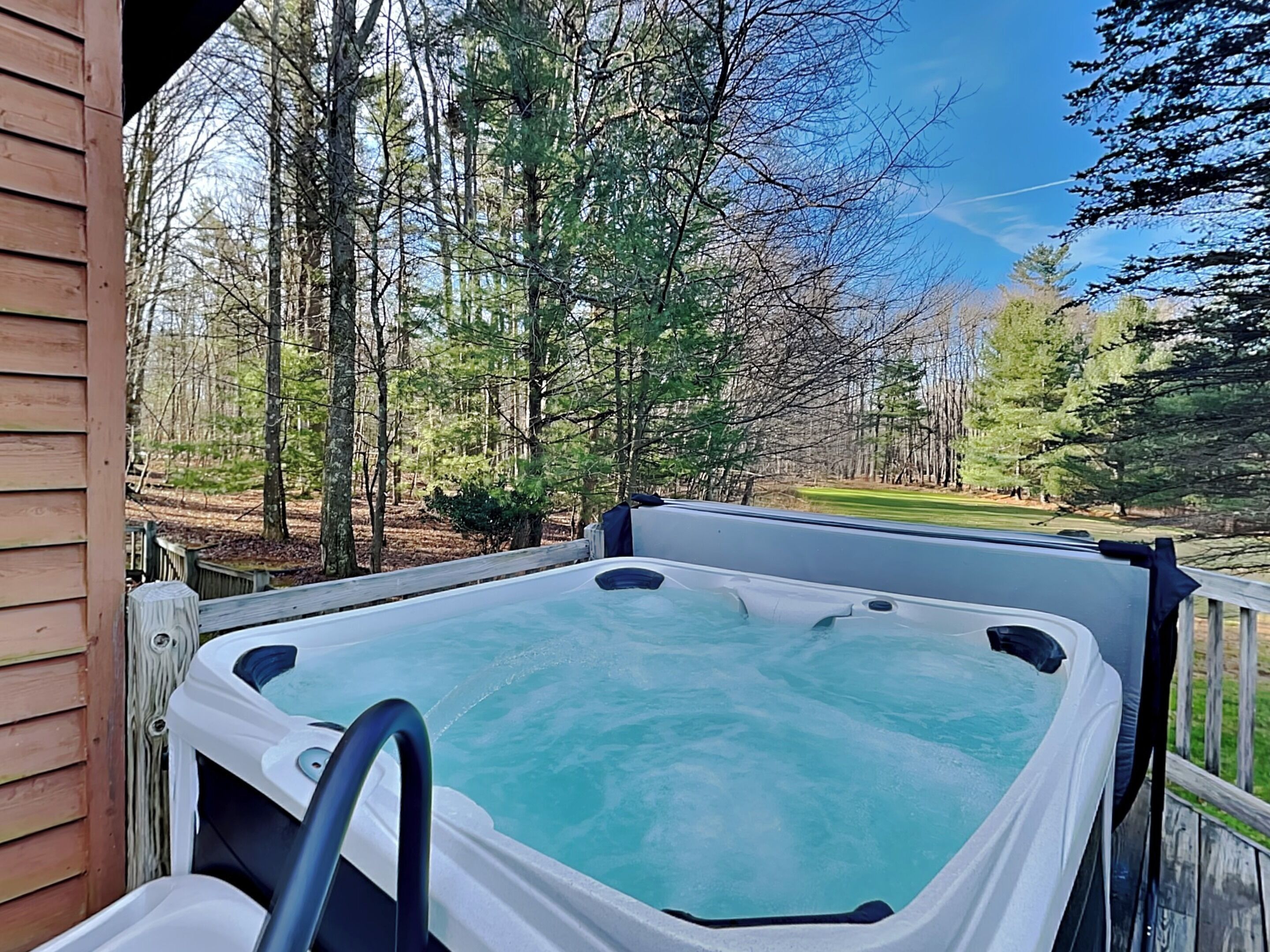 A hot tub on a wooden deck with a view of a forest and a golf course.