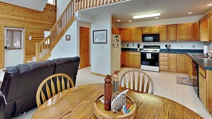 A cozy interior with a dining table, wooden chairs, a black leather sofa, a wooden staircase, and a kitchen with wooden cabinets and appliances. - Almost Heaven (Swanton)