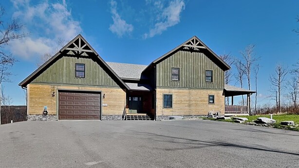 A two-story wooden house with a garage, a covered porch, and a stone foundation.