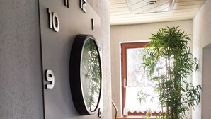 A hallway with a wall-mounted number plate, a potted plant, and a window with a view of the outside. - Vacation apartment in the Franconian Forest (Nordhalben)