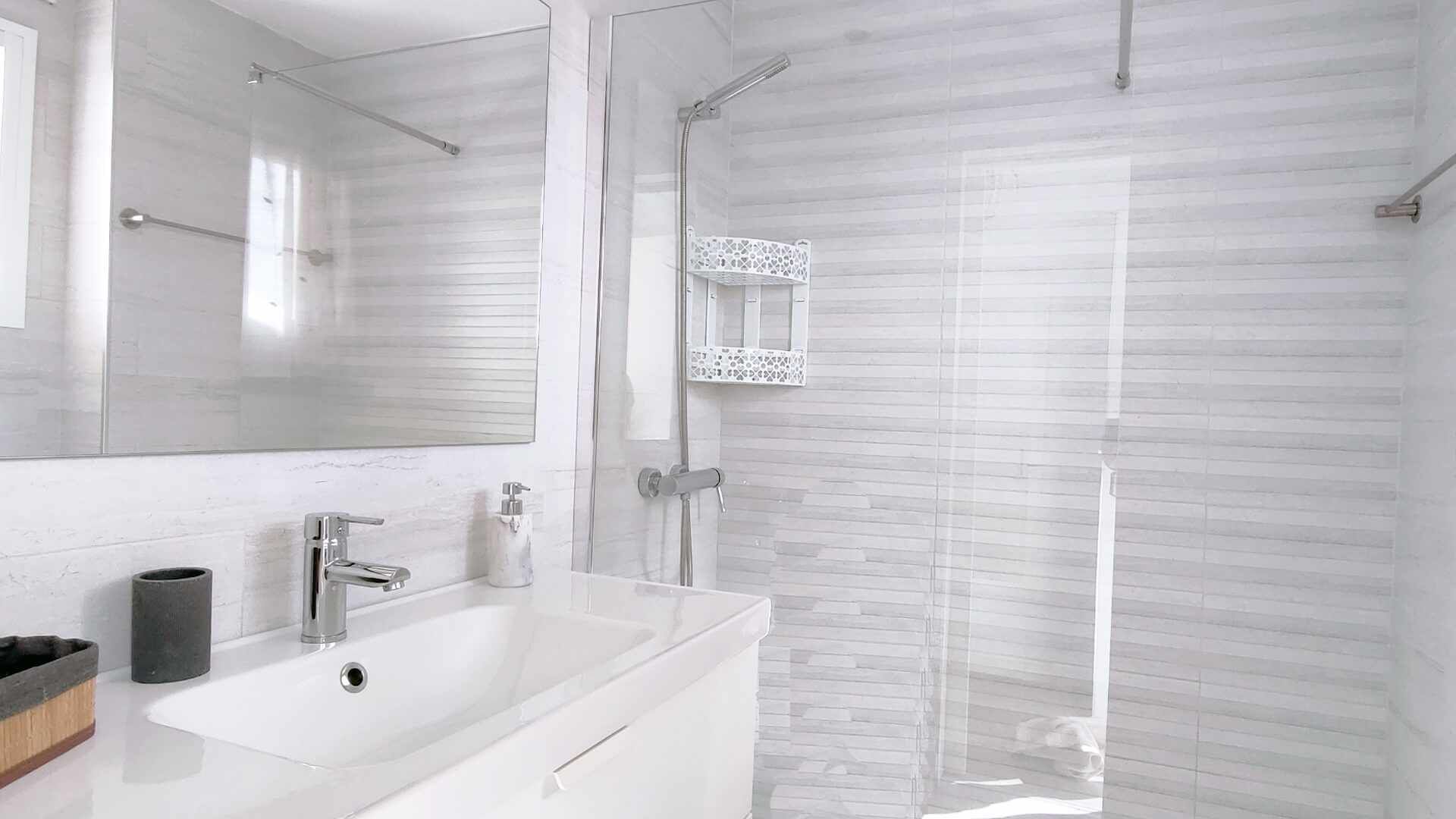 A modern bathroom with a white sink, a mirror, a shower with a glass door, and a toilet.