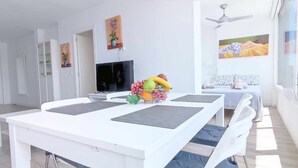A modern dining area with a white table, a fruit bowl, and a television. - Skyline Tower (Torre del Mar)