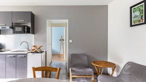 A modern kitchen with a microwave, a dining table with chairs, a grey sofa, and a small wooden table.