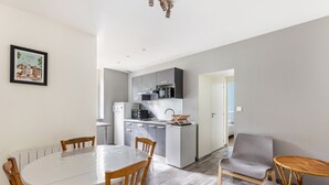 A modern kitchen with a dining area, a small island, and a seating area with a chair and a table.