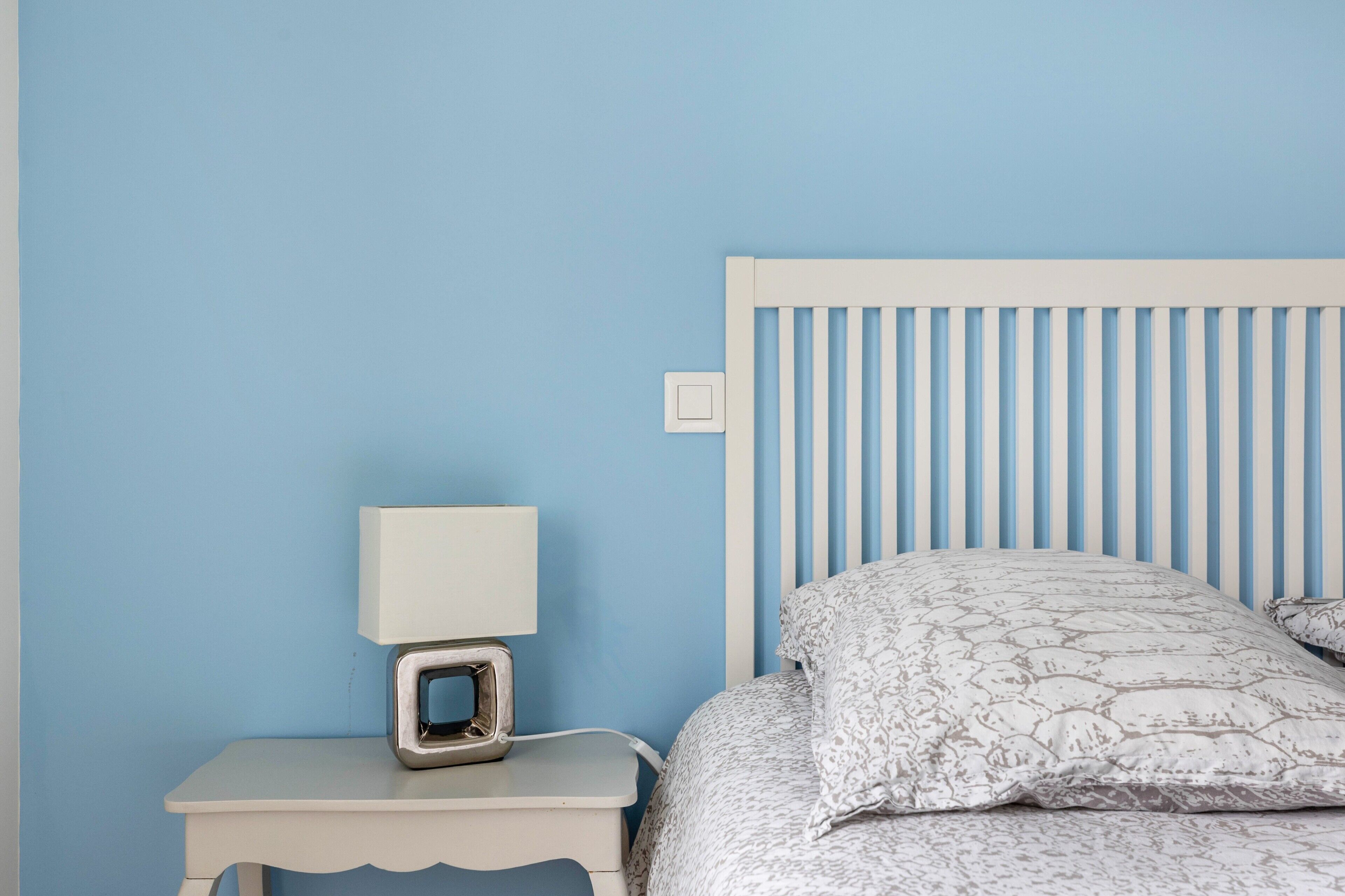 Una camera da letto con un letto, un comodino, una lampada e un interruttore a muro.