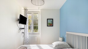 A bedroom with a bed, a TV mounted on the wall, a window with curtains, a radiator, and a framed picture on the wall.