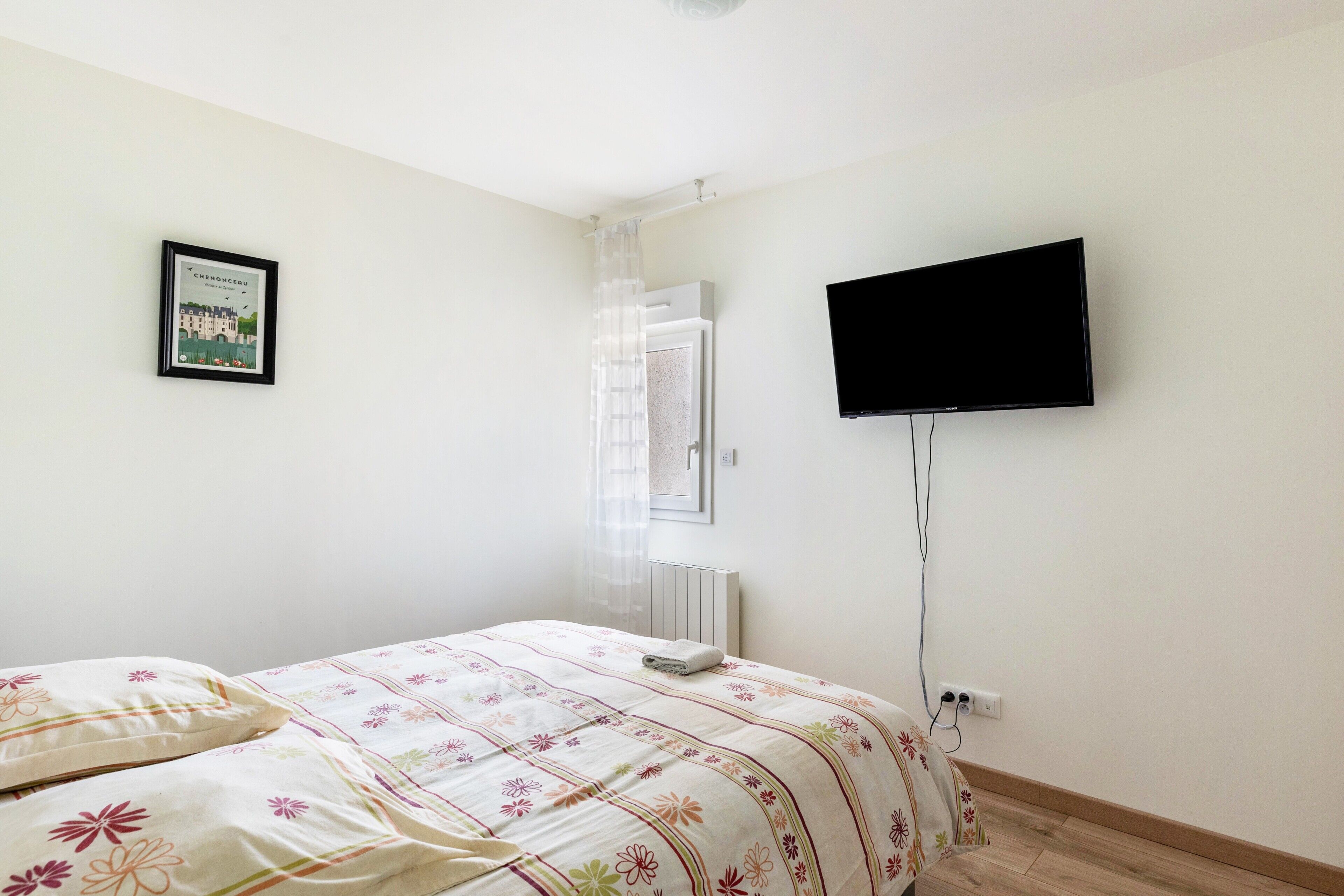 Une chambre à coucher avec un lit, un téléviseur, un radiateur et un tableau encadré au mur.