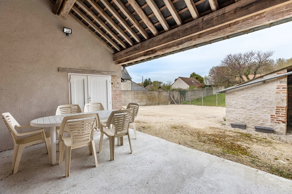 An outdoor patio with a concrete table and chairs, a wooden pergola, and a brick wall.
