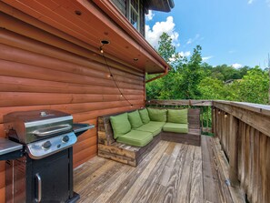 Una terraza de madera con una parrilla y un área de estar acolchada de color verde.