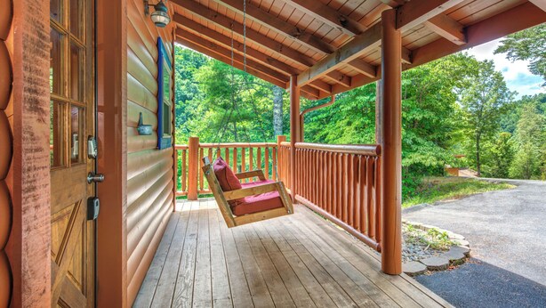 A wooden porch with a swing, a door with a keypad, and a view of a forested area. - Alexas Hideaway (Gatlinburg)