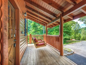 A wooden porch with a swing, a door with a keypad, and a view of a forested area. - Alexas Hideaway (Gatlinburg)