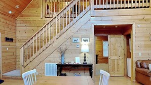 A wooden cabin interior with a staircase, a dining table with chairs, a lamp, and a couch. - Alexas Hideaway (Gatlinburg)