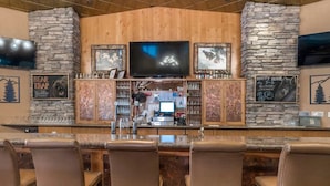 Zona de bar con paredes de piedra, un televisor de pantalla plana y taburetes.