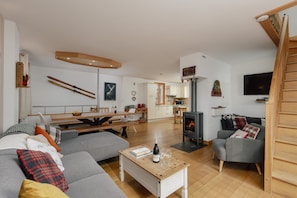 A modern living room with a sofa, a coffee table with a bottle and glasses, a fireplace, and a kitchen in the background. - Simply Morzine - Chalet Coeur (Morzine)