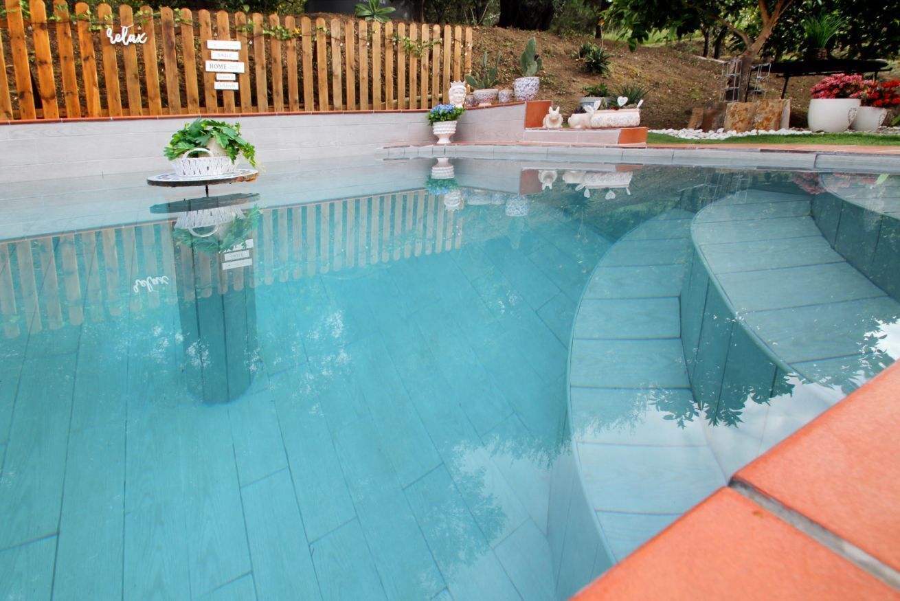 Une piscine entourée d’une clôture en bois, agrémentée de plantes en pot et d’un banc.