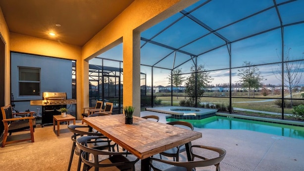 Eine geräumige Terrasse mit Holztisch und -stühlen, einem Grill und Blick auf einen Swimmingpool und die Landschaft.