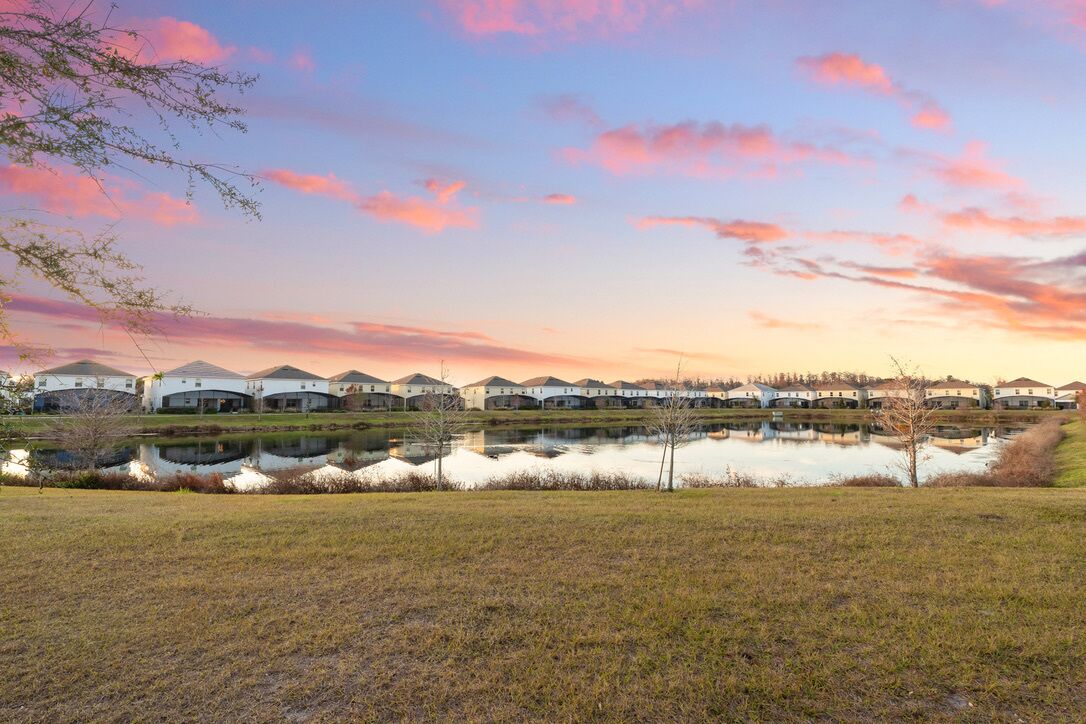 A row of white buildings with a reflective pond in front, under a sunset sky.
