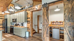 A rustic kitchen with wooden beams, a large island, and a sliding barn door leading to a dining area.