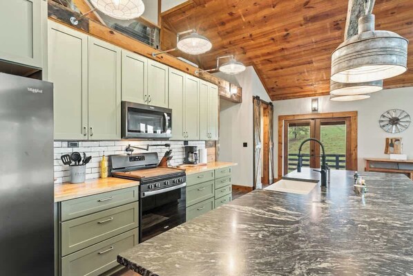 A kitchen with a large island, wooden ceiling, and modern appliances. - 10-Acre Farm Retreat w/ Hot Tub & Views (Ellijay)