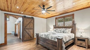 A bedroom with a wooden ceiling, a large bed with a headboard, a nightstand, and a sliding barn door.