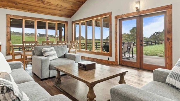 A spacious living room with a wooden ceiling, large windows, and a view of a green landscape.