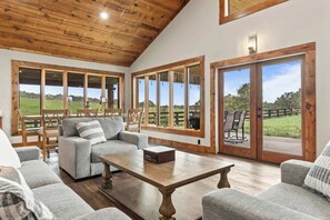 A spacious living room with a wooden ceiling, large windows, and a view of a green landscape.