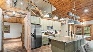 A spacious kitchen with a large island, stainless steel appliances, and a wooden ceiling.