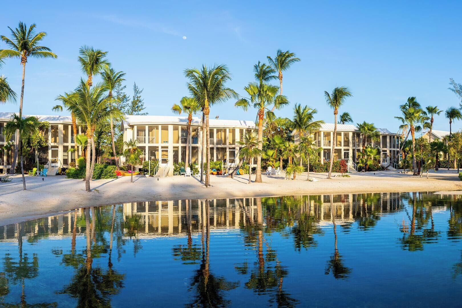 A resort with multiple-story buildings, palm trees, and a calm water body reflecting the structures.