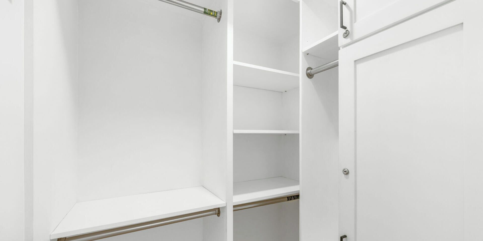 A white closet with open doors, revealing shelves and hanging rods.