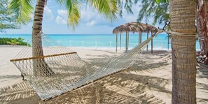 A hammock tied to a tree on a sandy beach with a thatched-roof structure in the background. - SeaBreeze 3 on 7 Mile Beach (Seven Mile Beach)