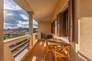A balcony with a wooden table and chairs, a view of buildings and mountains, and a tiled floor. - 'Golfo Aranci Nel Cuore' Apartment with Balcony, Wi-Fi and Air Conditioning (Golfo Aranci)