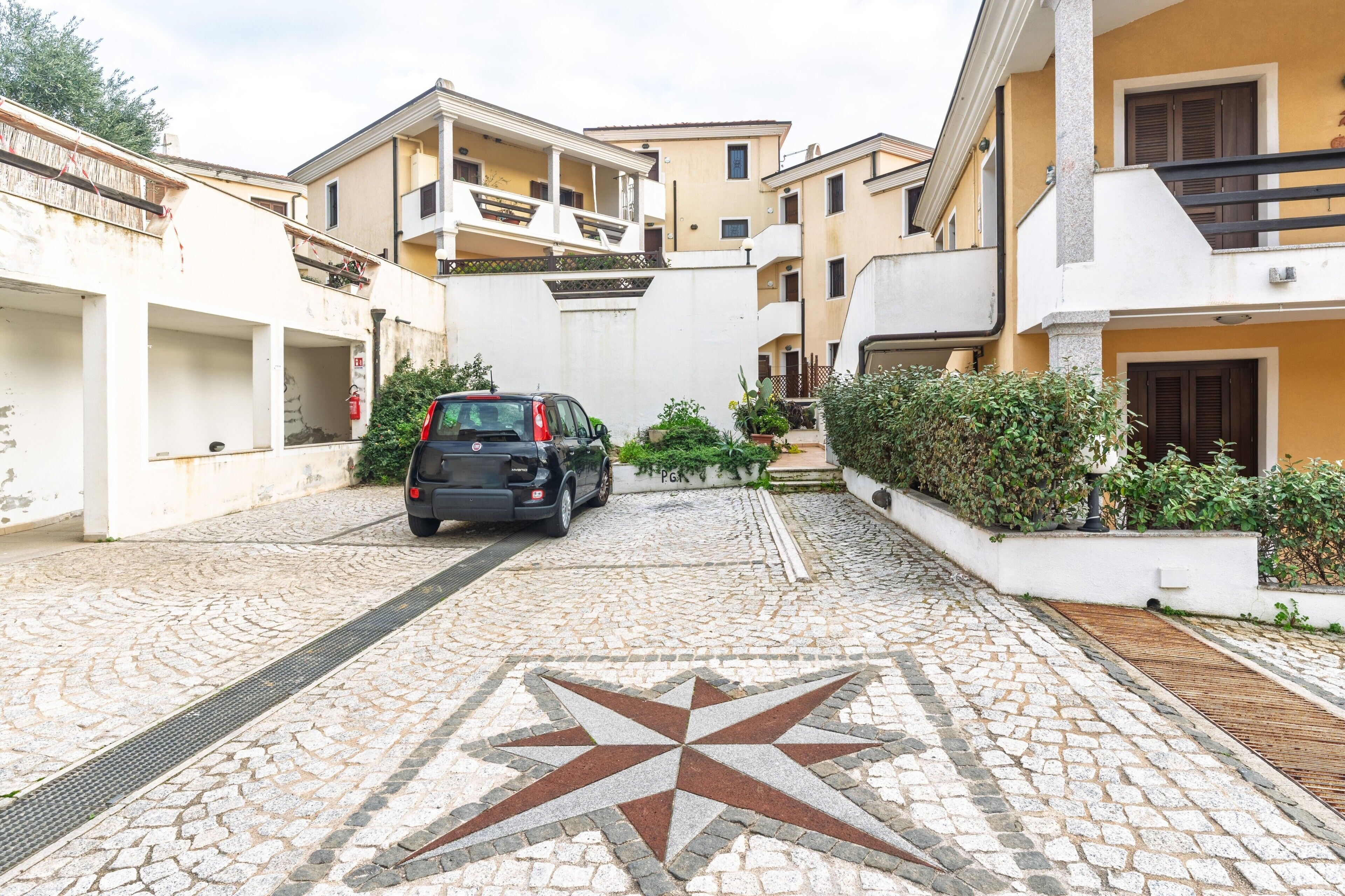 A paved street with a star-patterned tile, a parked car, and multi-story buildings with balconies.