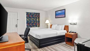 A hotel room with a bed, desk, chair, bedside table, lamp, and artwork on the wall.