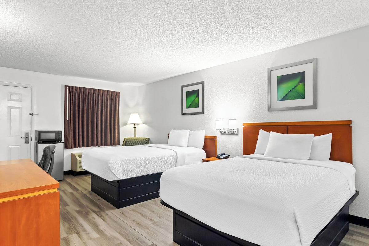 Habitación de hotel con dos camas, un escritorio, microondas, refrigerador y televisión.