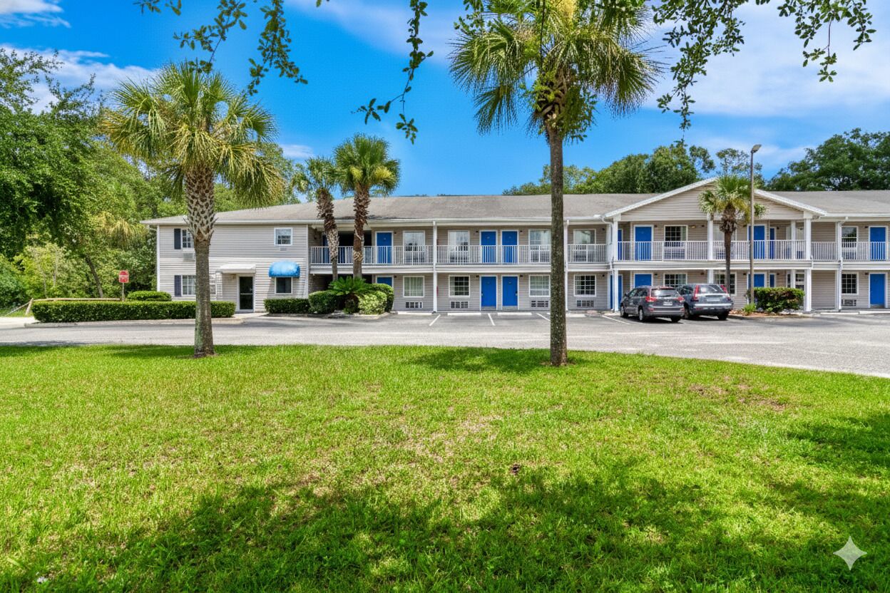 A motel with a two-story structure, a parking lot, and several palm trees.