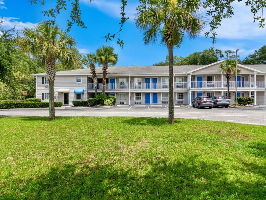 A motel with a two-story structure, a parking lot, and several palm trees.