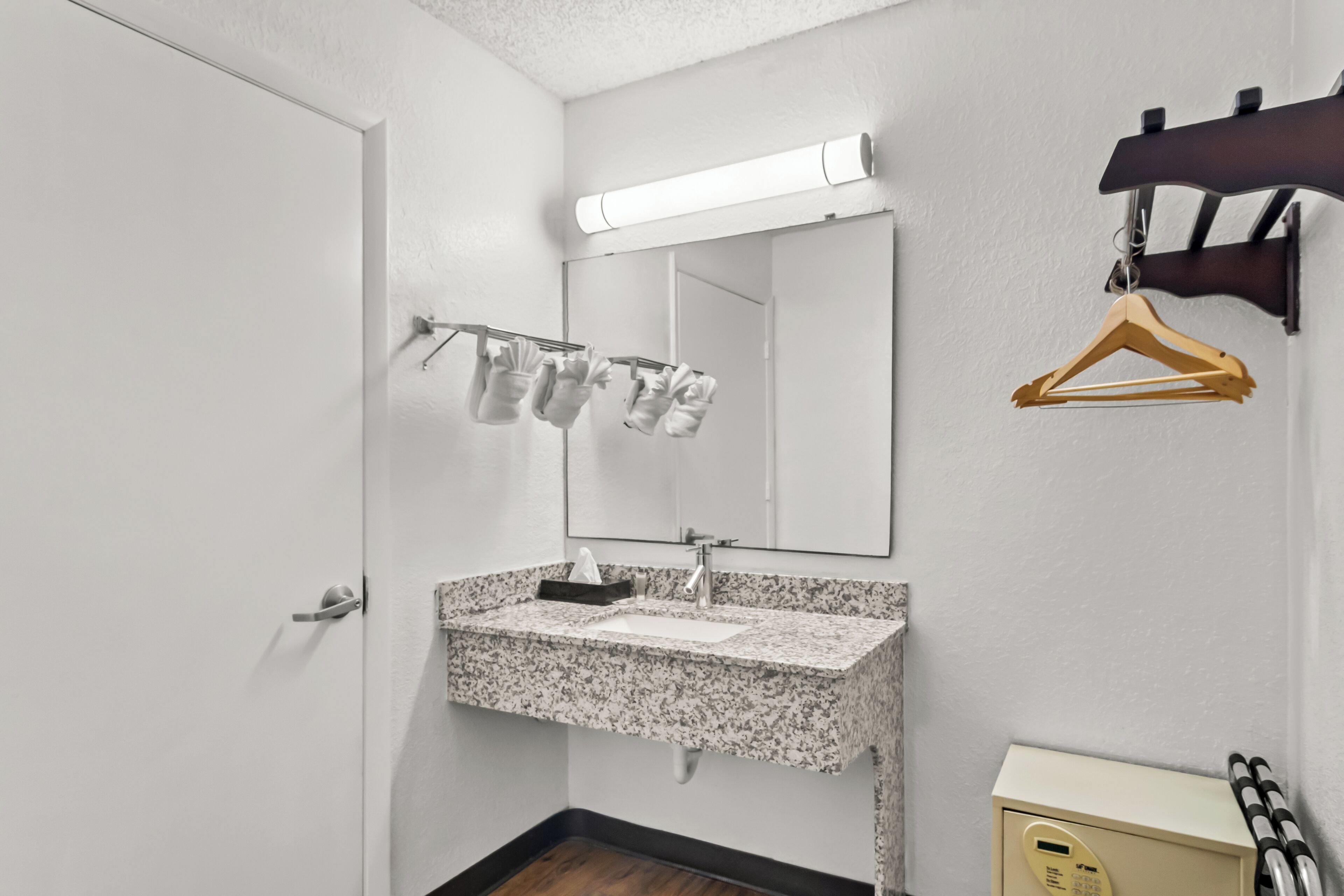 Un baño con lavamanos de encimera de granito, un espejo, toalleros con toallas, una percha de madera y un pequeño armario con cerradura digital.