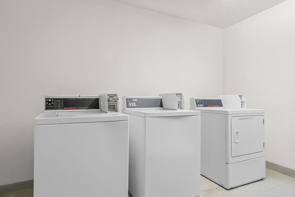 Une buanderie équipée de trois machines à laver et de trois sèche-linge blancs.