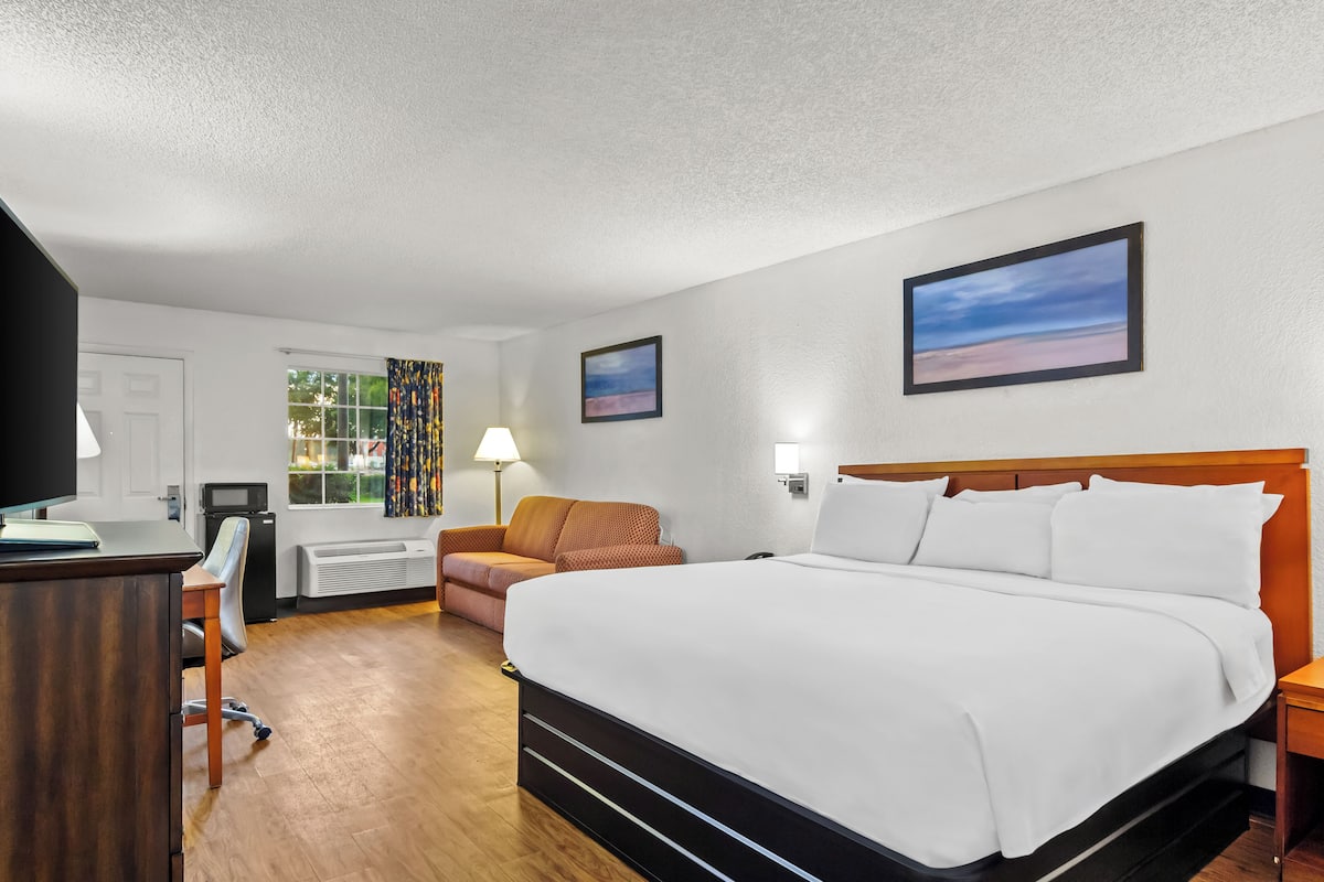 Habitación de hotel con una cama grande, un escritorio, una silla, un televisor y una ventana con cortinas.