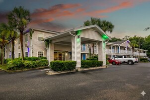 Un motel con entrada techada, palmeras y una camioneta estacionada en el estacionamiento.