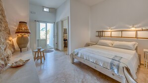 A bedroom with a bed, bedside tables, a lamp, and a stone wall. - Villa 'Camera 2' with Sea View, Private Pool and Wi-Fi (Lido Marini)