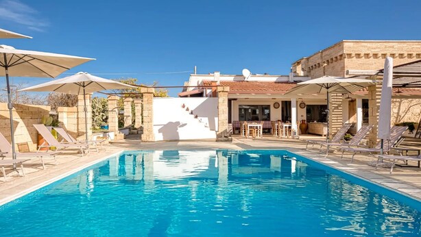 En swimmingpool med solstolar och parasoller, en byggnad med ett tak täckt av tegelpannor och en satellantenn.