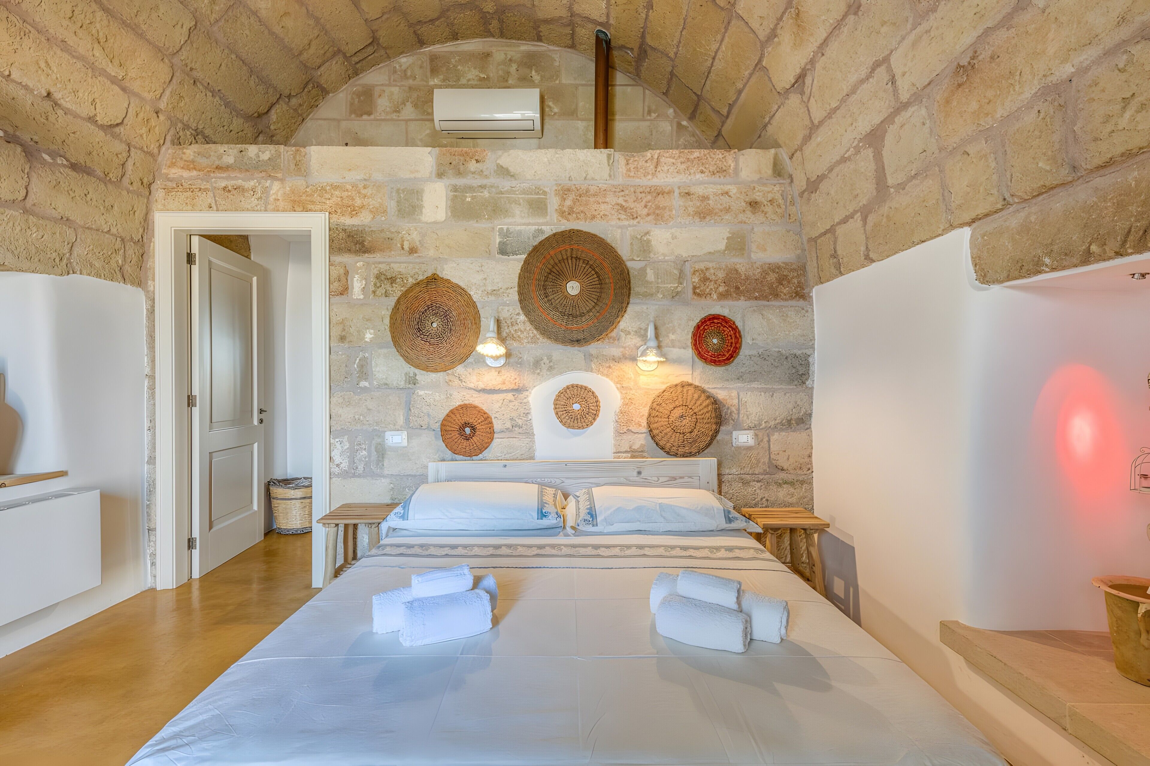 A room with a stone wall, a bed with white linens, and three woven wall hangings.